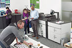 Fotografía de gente trabajando en una oficina con varias impresoras industriales a su lado