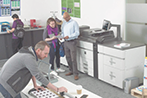 Fotografía de gente trabajando en una oficina con varias impresoras industriales a su lado